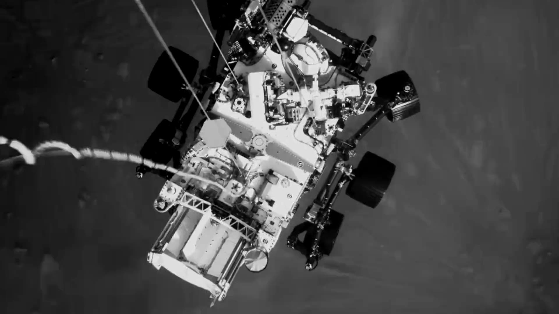 NASA'nın Perseverance aracı, iniş halatlarıyla gök vincinin altında asılı; Mars yüzeyinin hemen üzerinde, aşağıdan toz yükseliyor.